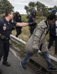 Френски полицаи ескортират мигранти от Еритрея на пътя, недалеч от Кале и тунела под Ламанша. Сн.: EPA/БГНЕС