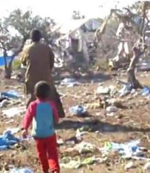 Мъж и дете от лагера вървят сред отломки и унищожени палатки. Сн.: Скриншот видео YouTube